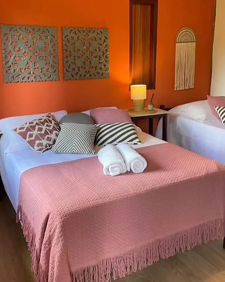 Apartamento com cama de casal e cama de solteiro, parede terracota e enxoval rosa